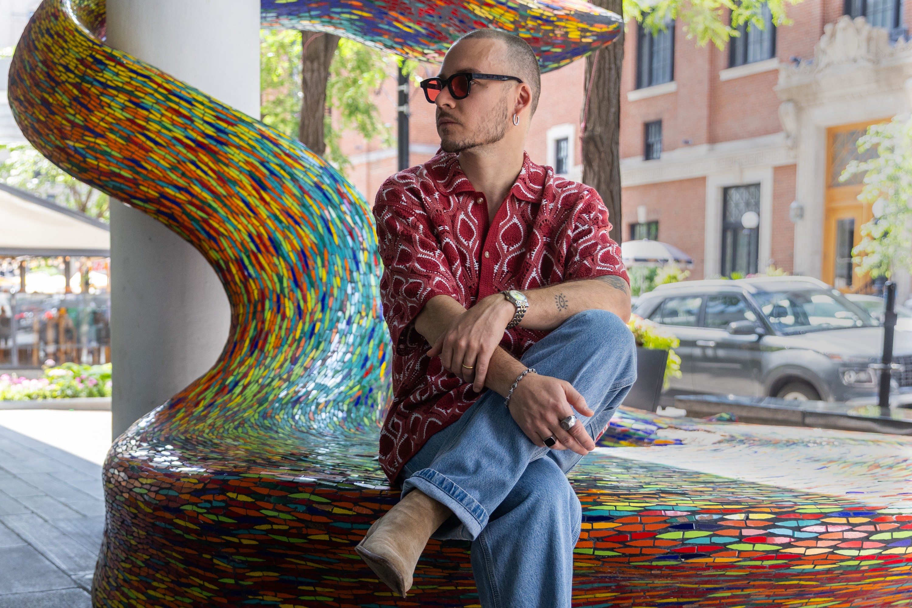 A man sits on the edge of an artwork on a sidewalk.
