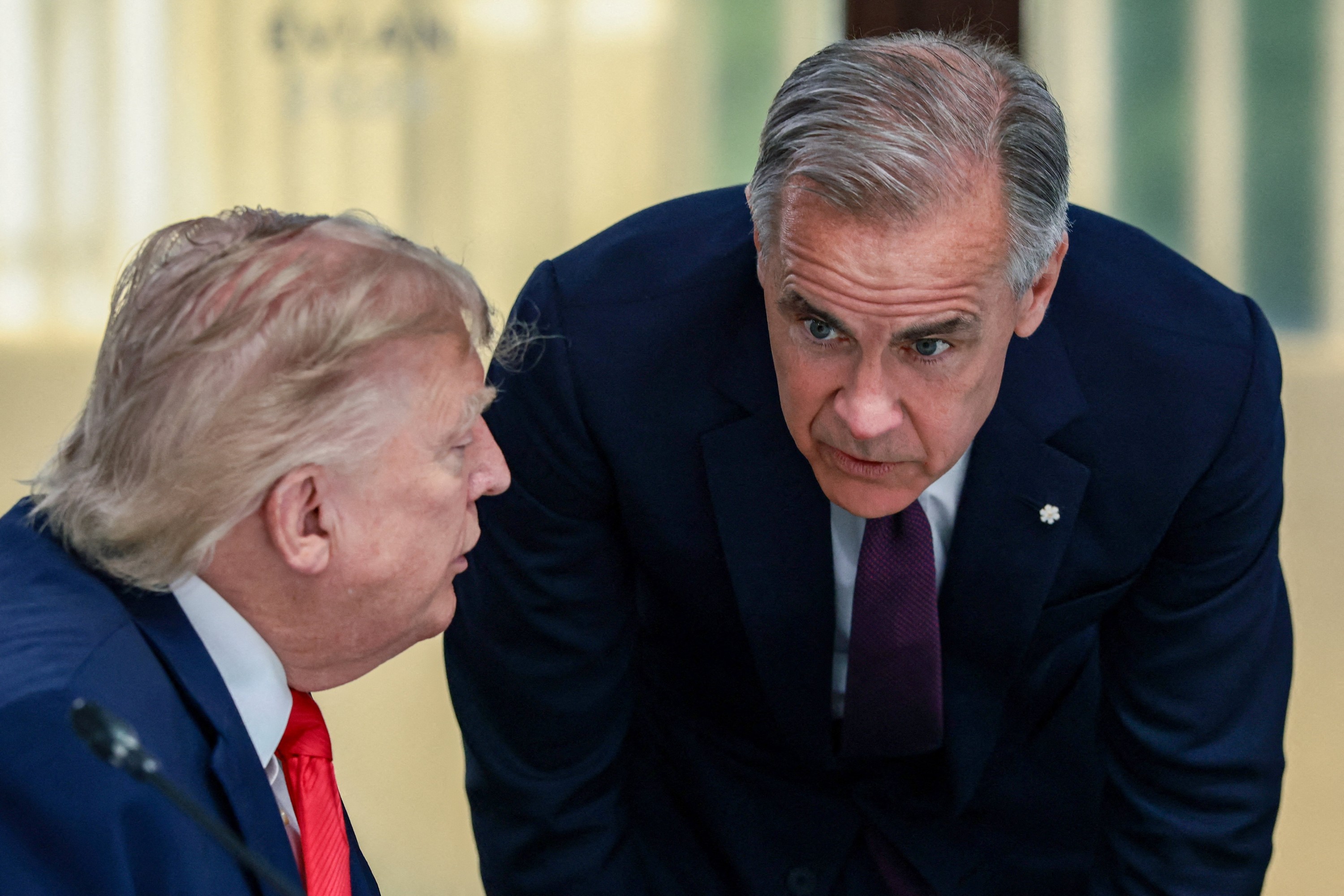 Prime Minister Mark Carney bends to listen to a sitting Donald Trump during a work lunch at the G7 summit in France 