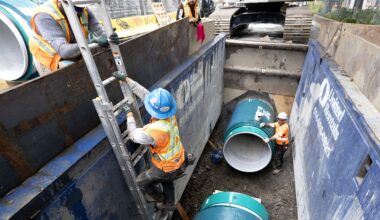 Workers in trench with big water main pipes.