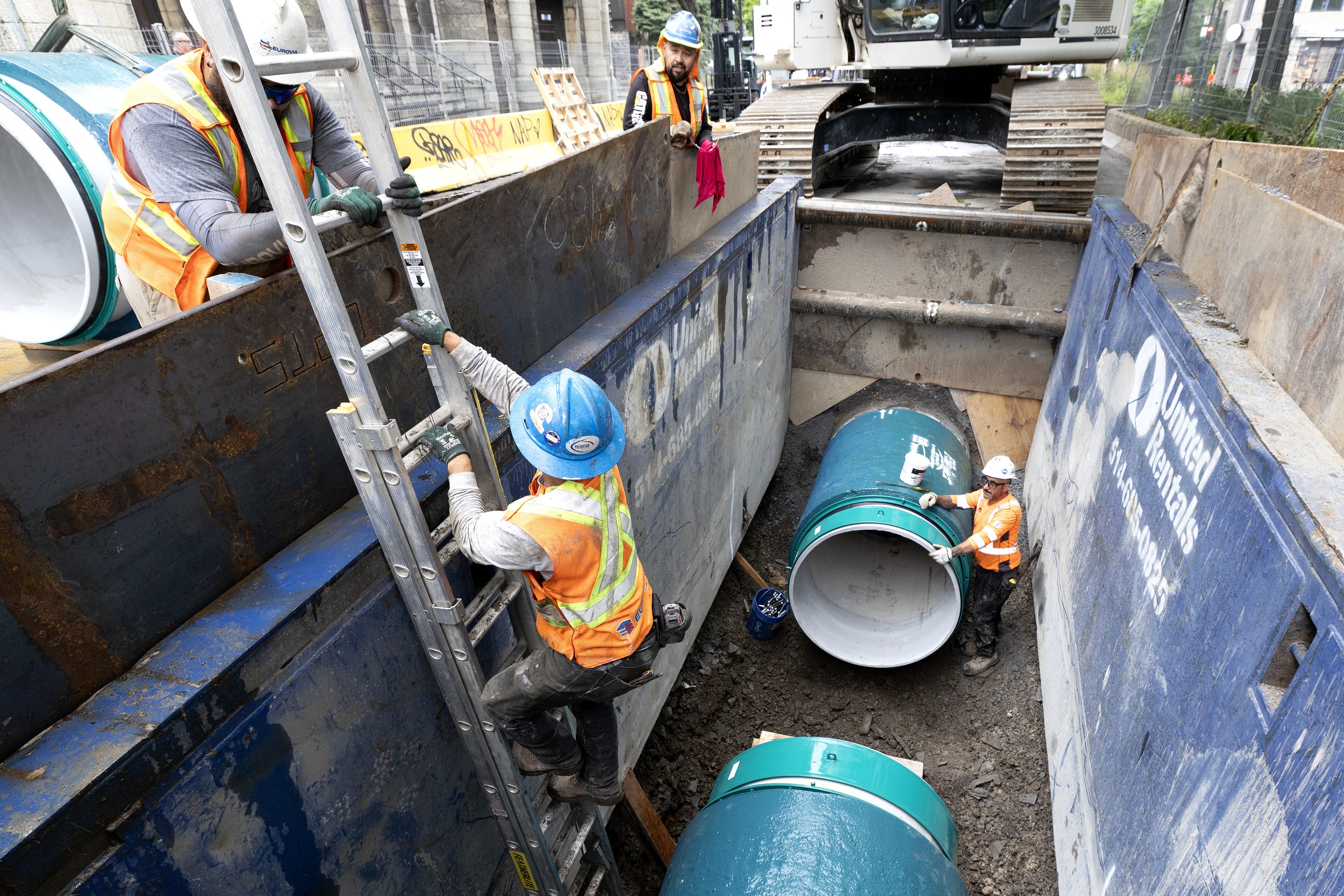 Workers in trench with big water main pipes.