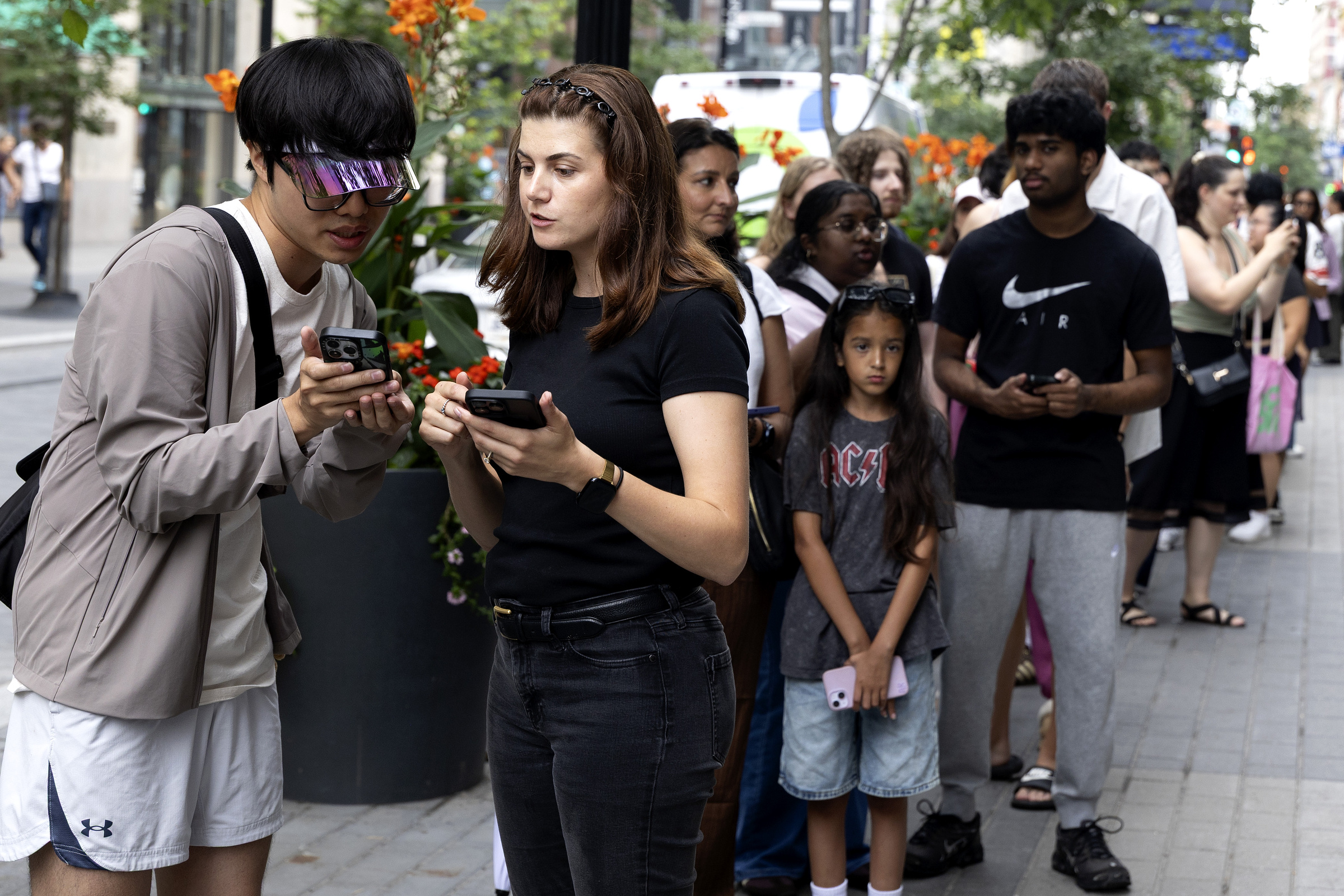 A man checks a woman's phone at the front of a lineup on a downtown street.