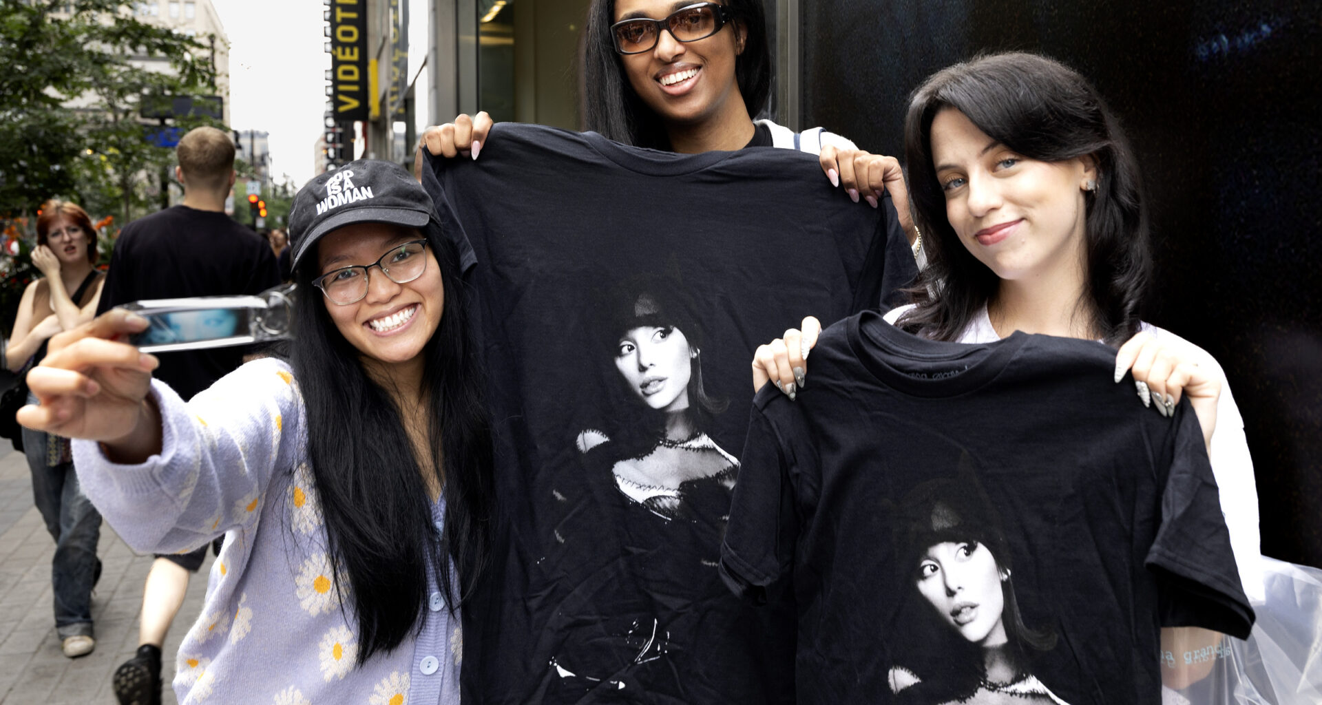 Two young women hold up black T-shirts with Ariana Grande