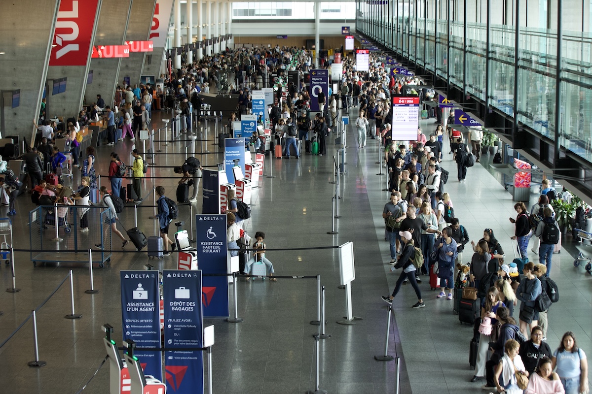 From above, hundreds of people are seen packed into lineups at an airport.