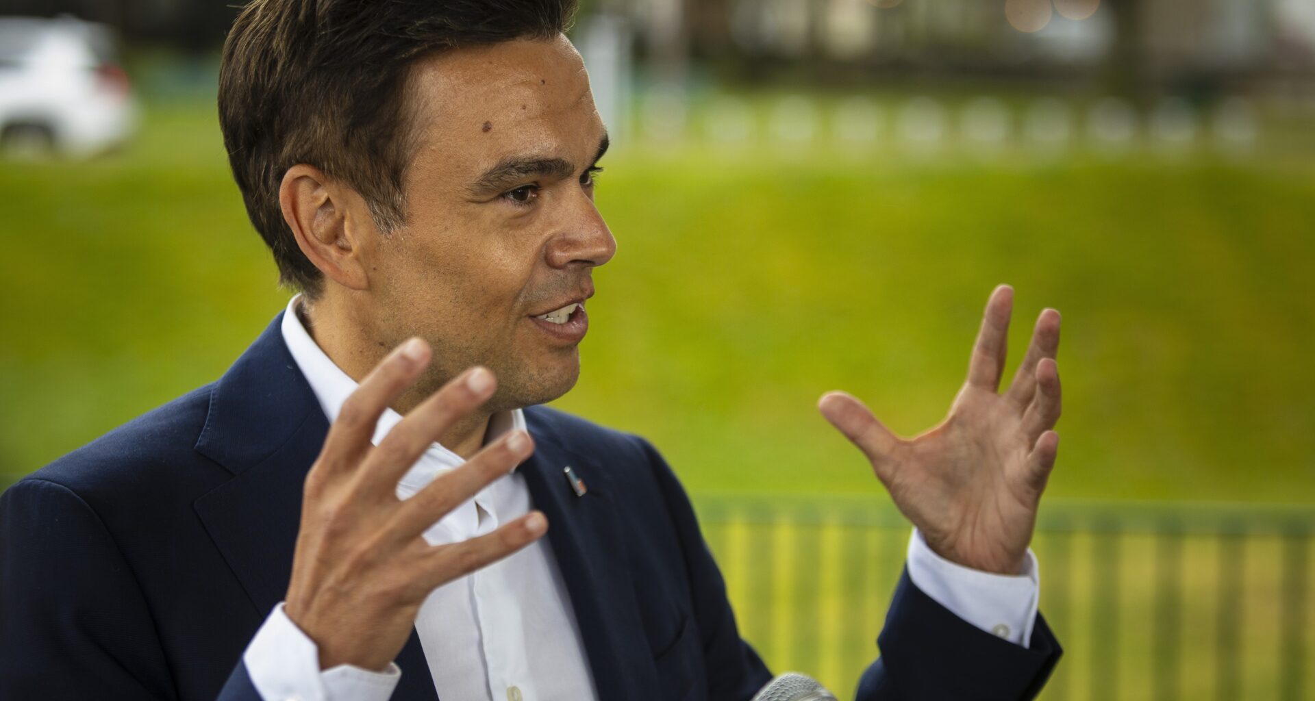 Quebec Liberal Leader Charles Milliard gestures as he speaks into a microphone in front of a grassy area