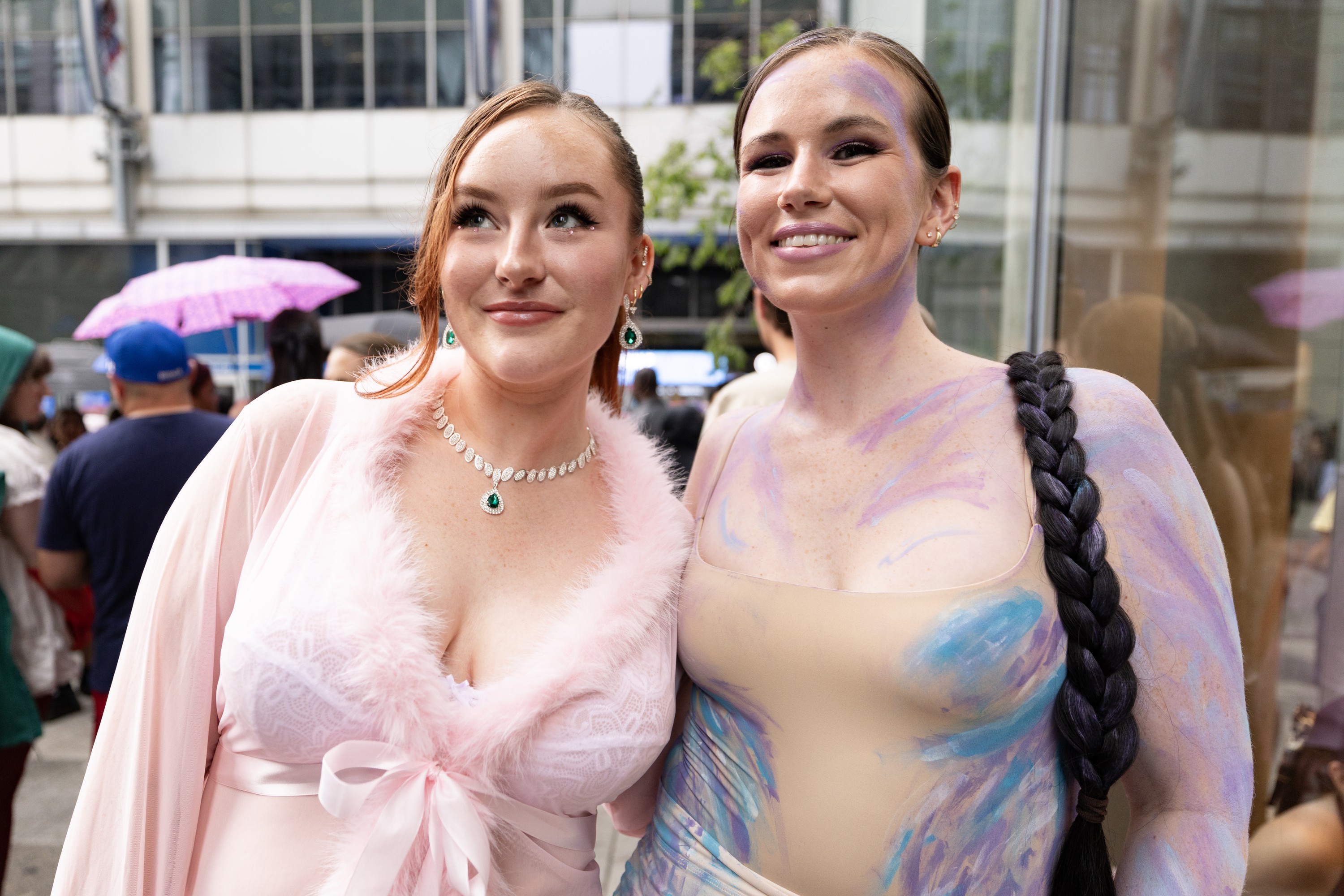 Two young women in stylish outfits and makeup smile as they stand on a street