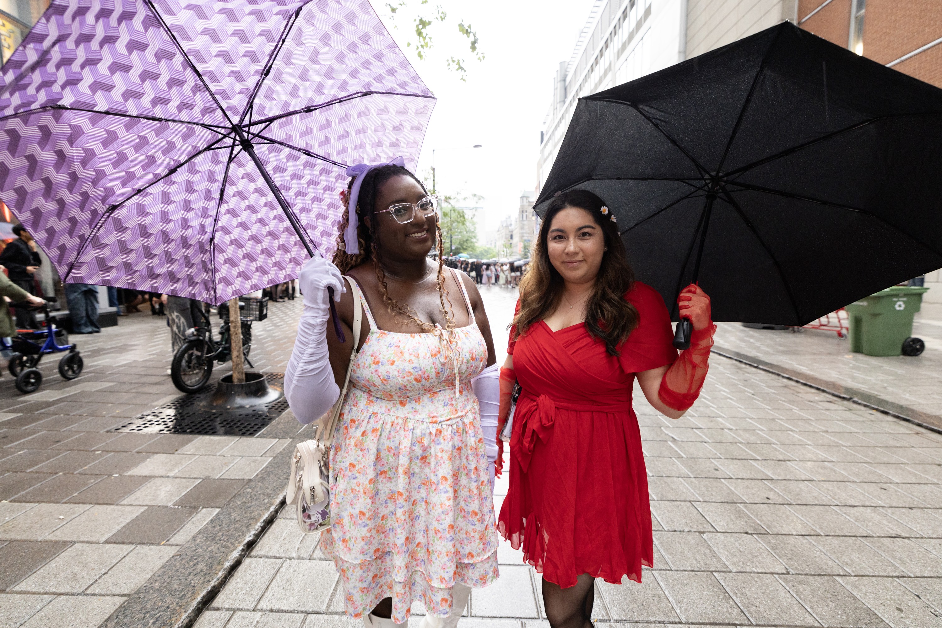 Two young women stand under umbrellas on a rainy street