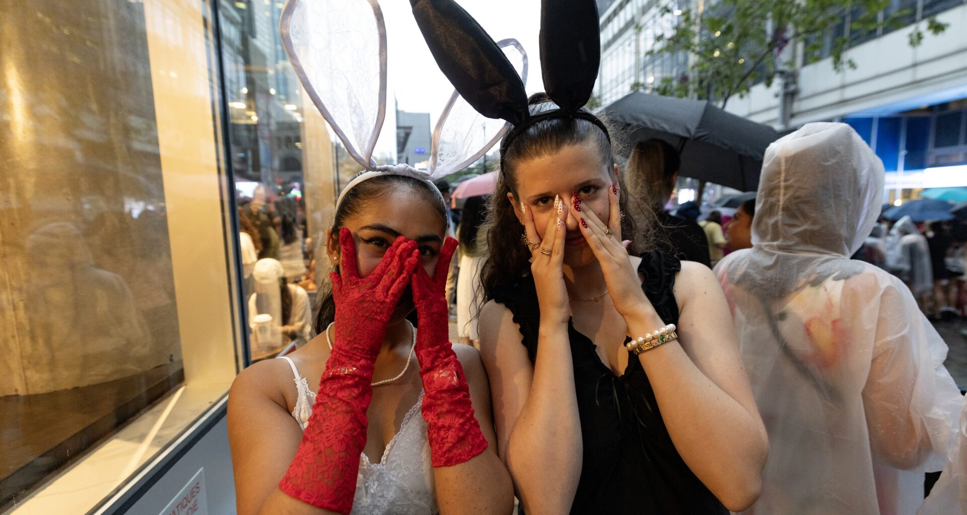 Two young women peek through their fingers while wearing rabbit-ear headpieces