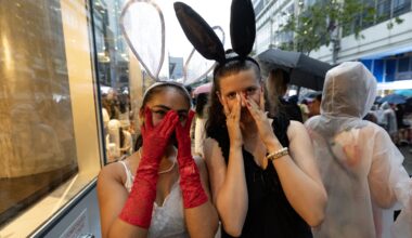 Two young women peek through their fingers while wearing rabbit-ear headpieces