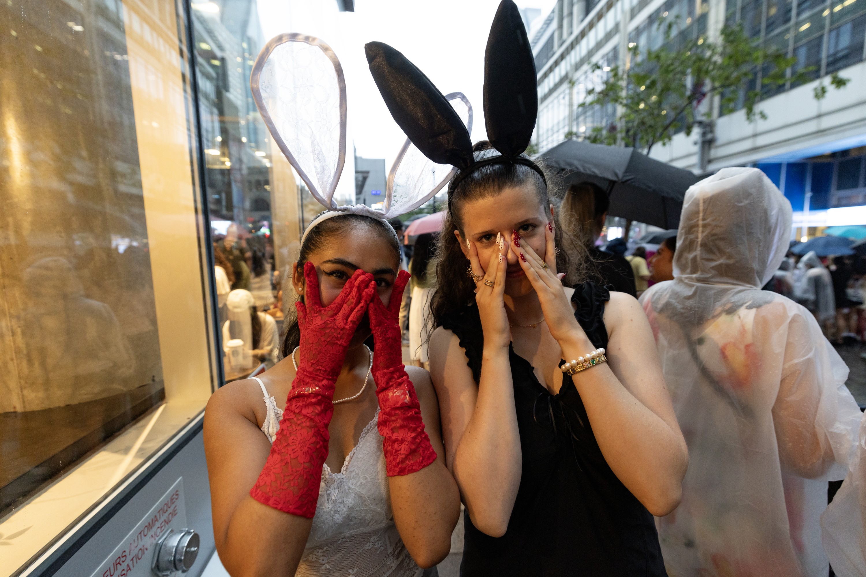 Two young women peek through their fingers while wearing rabbit-ear headpieces