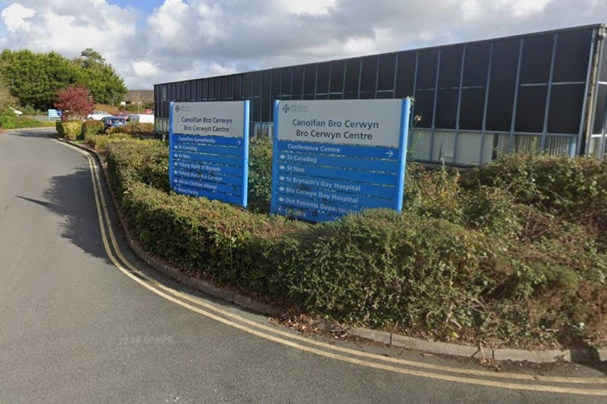 A low, black modern-looking office building. In front of the building is a sign saying 'Bro Cerwyn Centre' with arrows pointing to various departments and wards