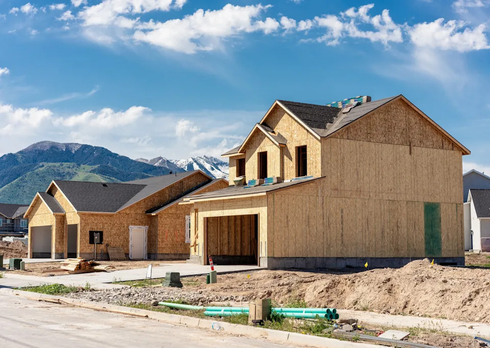 Two unfinished houses under construction in a suburban neighborhood, with mountains visible in the background