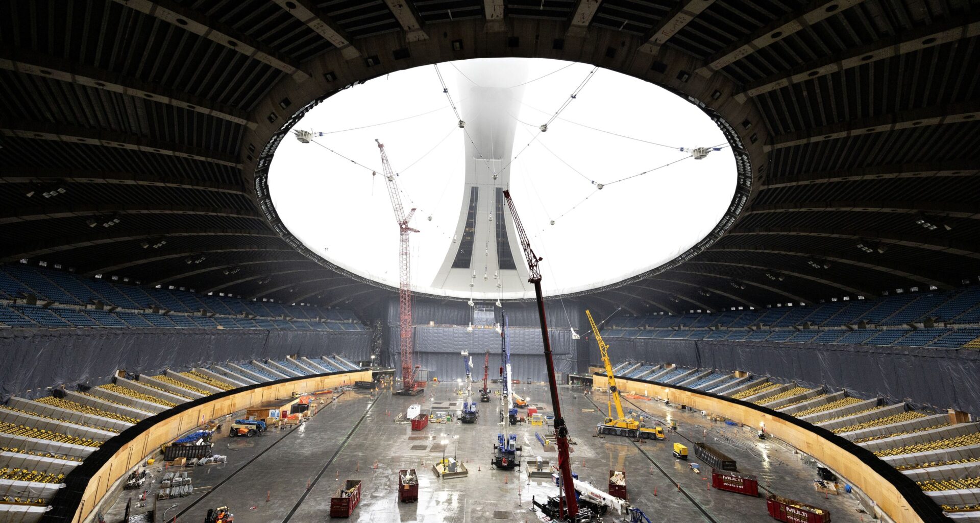 View from inside a roof-less Olympic Stadium of cranes and lifts with the stadium's tower in the background, shrouded in haze.