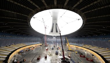 View from inside a roof-less Olympic Stadium of cranes and lifts with the stadium's tower in the background, shrouded in haze.