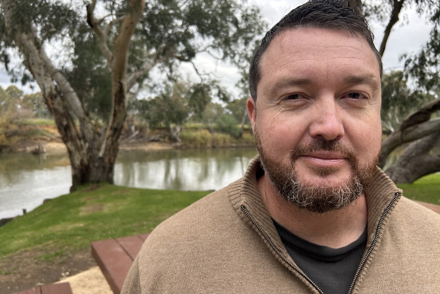 A man smiles at the camera in front of a river