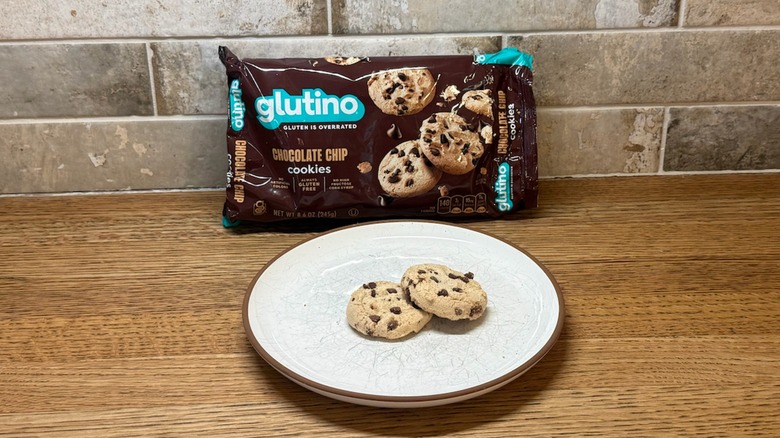 Two Glutino chocolate chip cookies on a plate with a package in the back