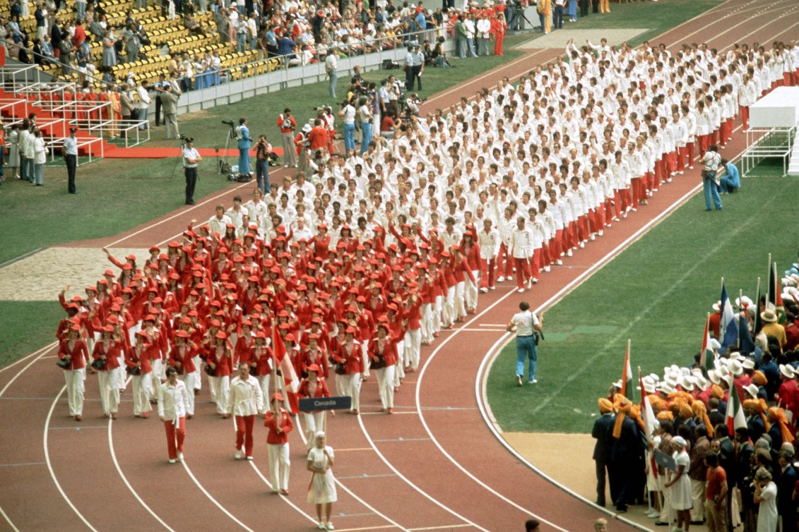 Athletes in red march ahead of athletes in white on a track