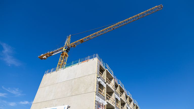 A crane above a block of flats under construction, seen against a blue sky.