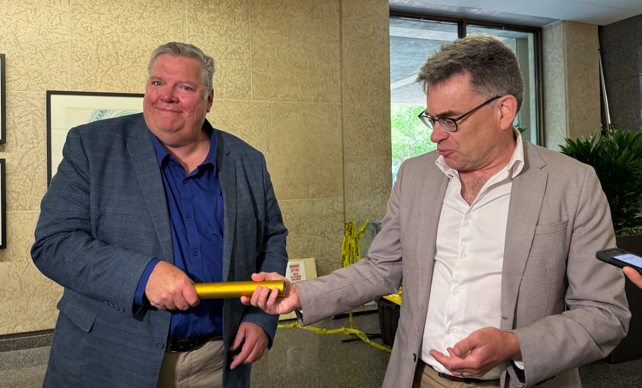 Two men wearing suits are holding a yellow baton.