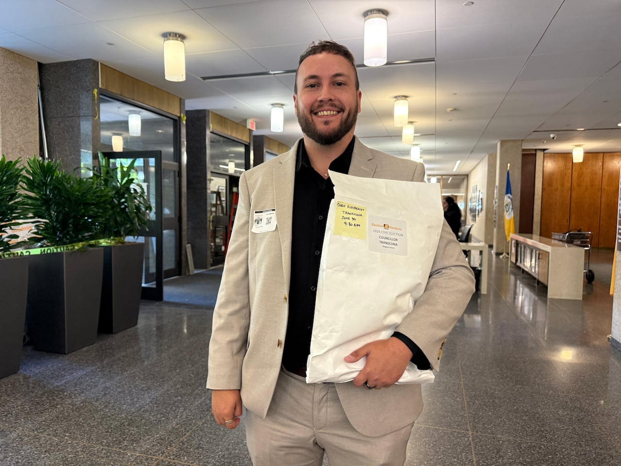 A man wearing a suit is standing and holding a large paper envelope.