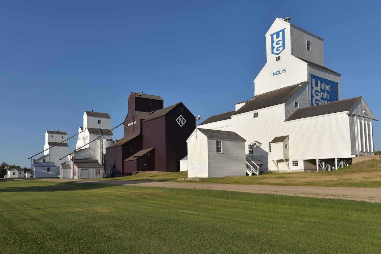 Brown and white grain elevators at the edge of a grassy field.