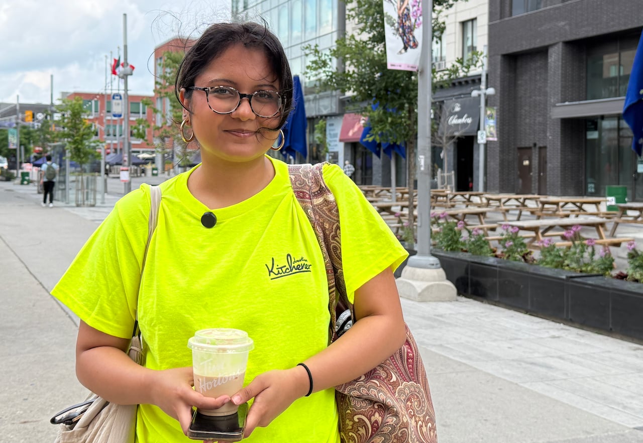 A woman in a yellow shirt on a downtown street holding an iced coffee