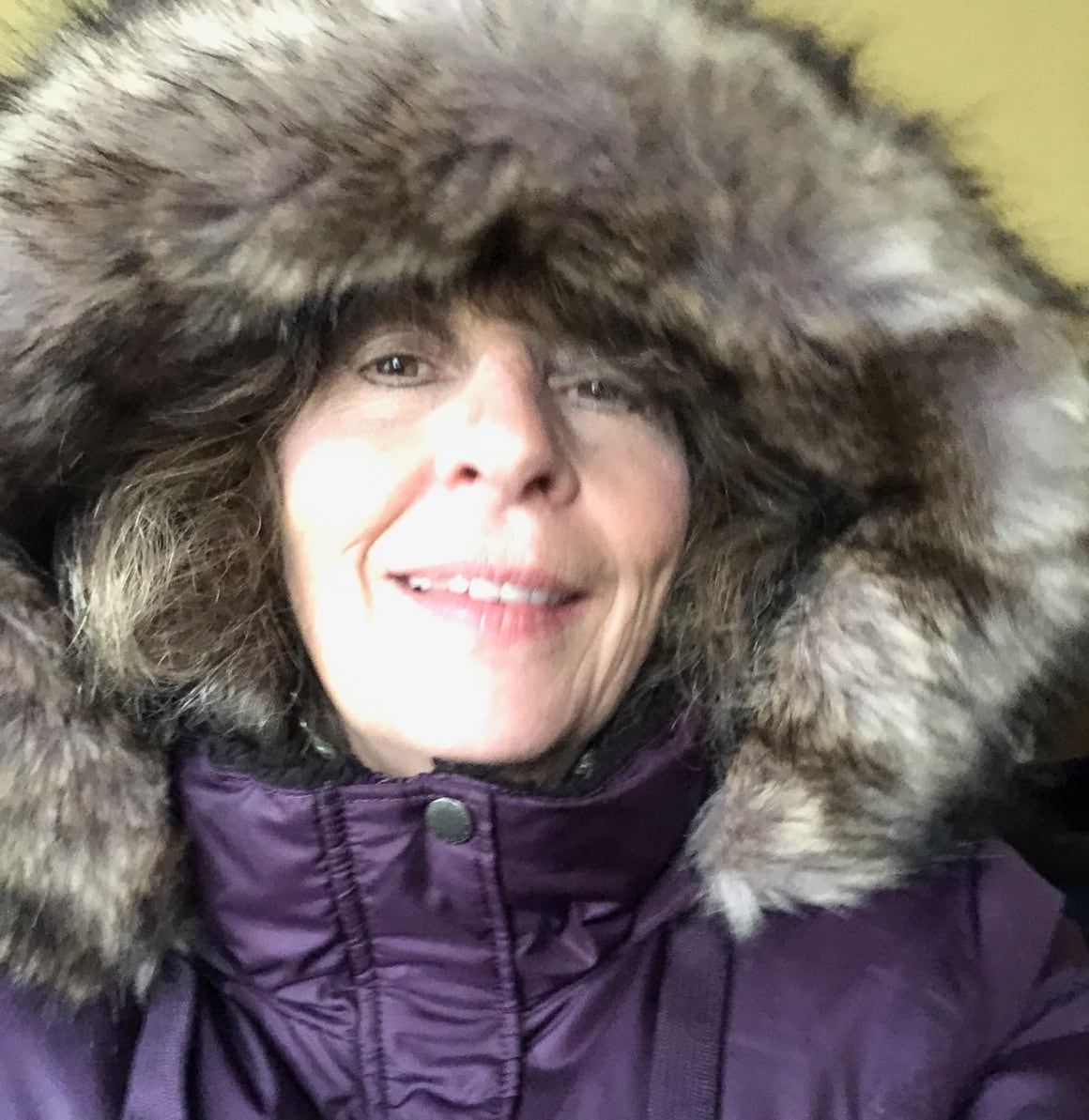 A close-up of a woman's face peaking out of the hood of a fur-lined parka.