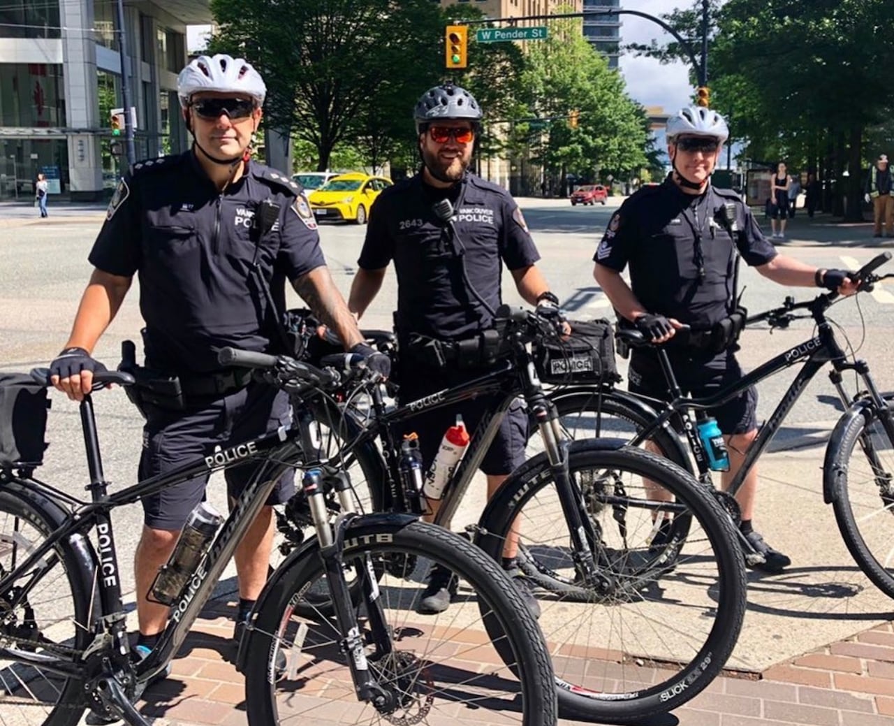 Three uniformed police officers smile next to bikes.