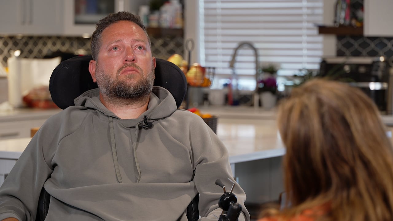 A man with tears in his eyes in a wheelchair looks up.
