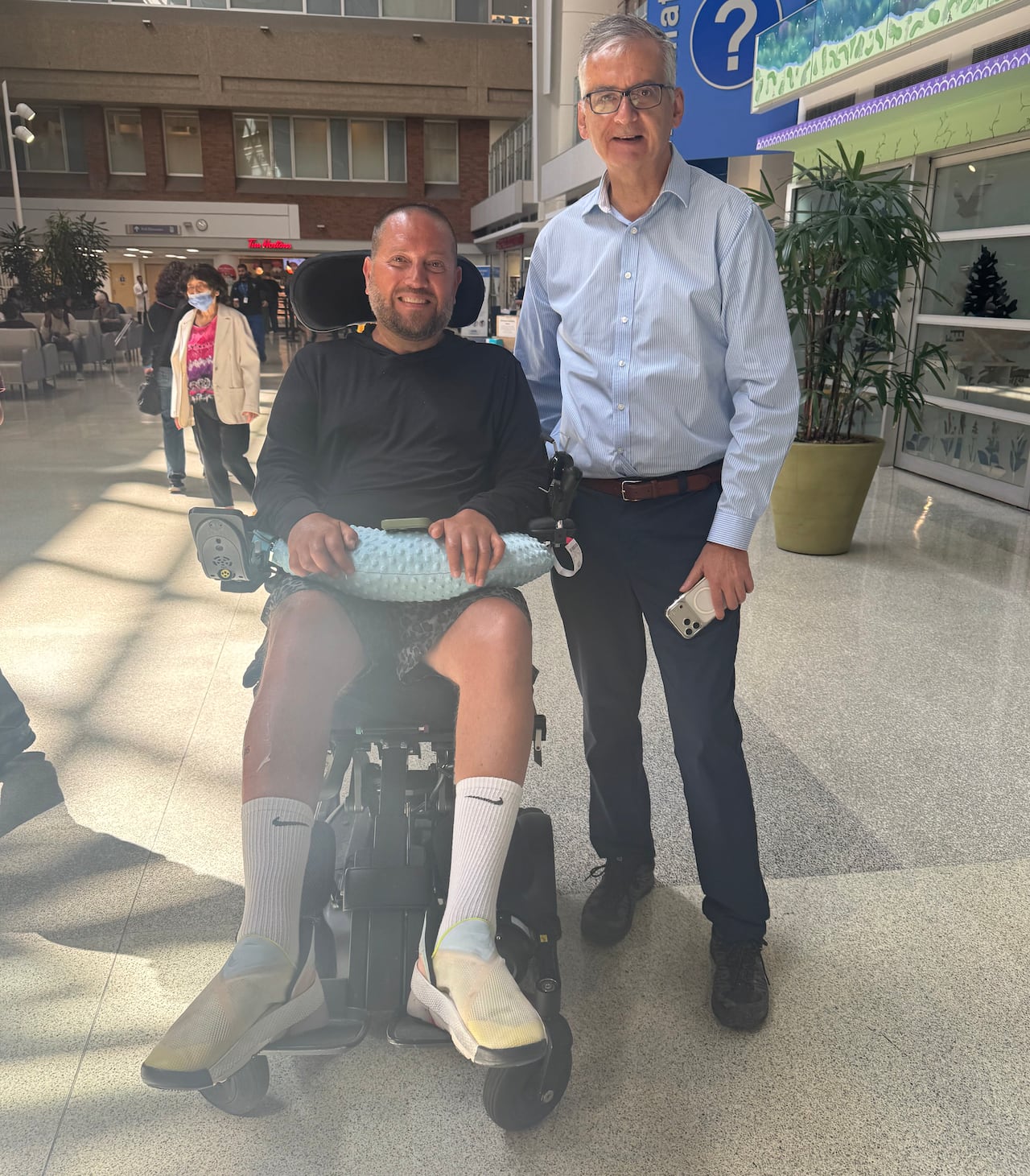 A man in a wheelchair smiles next to a man wearing a blue shirt.