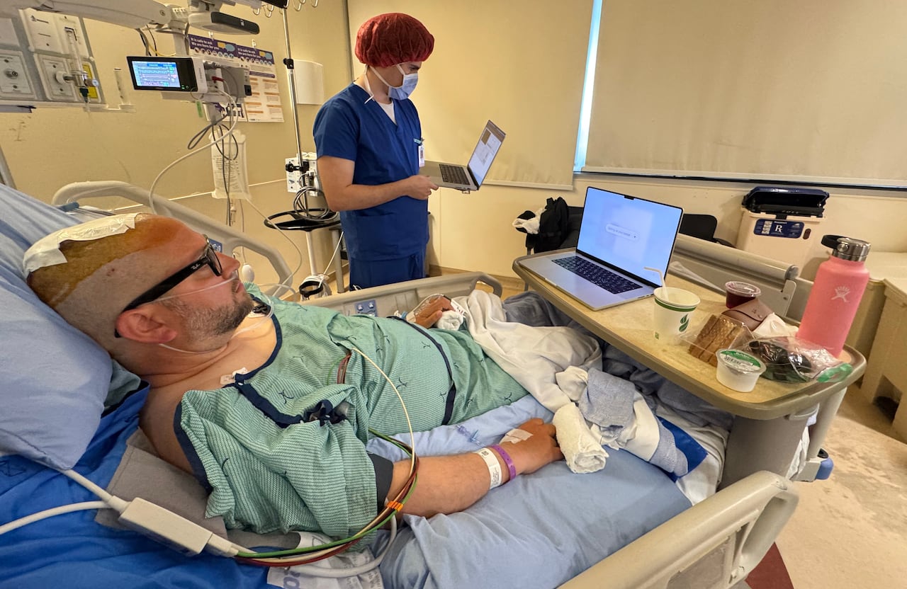 A man with a head bandage is seen in a hospital bed.
