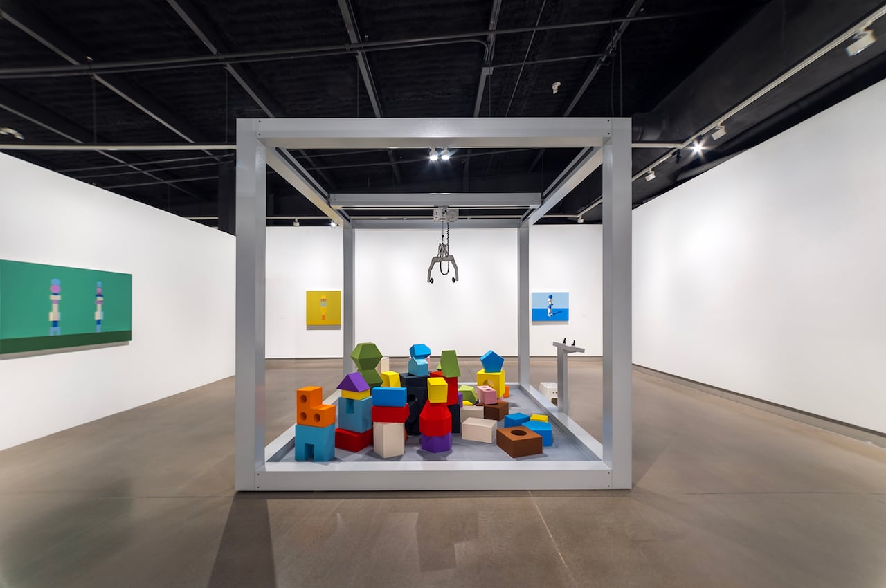 Inside a white-walled gallery sits a giant sculpture in the shape of a claw machine full of colourful blocks.