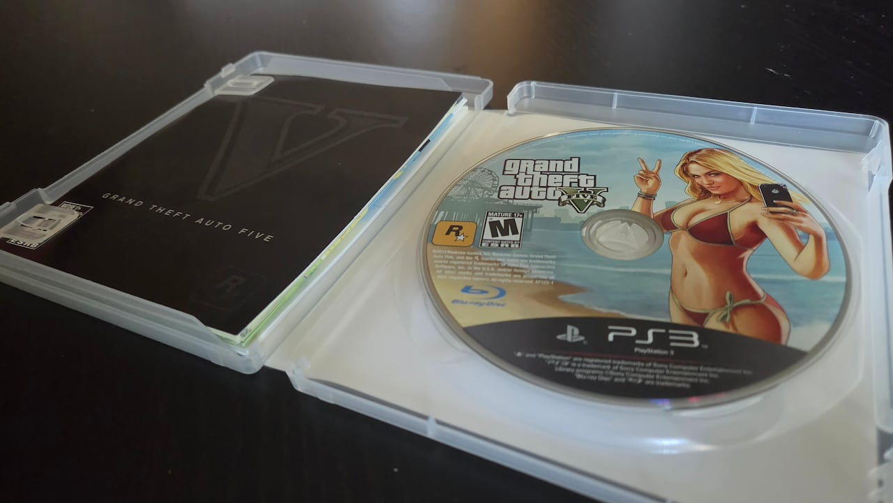 A disc case lies open, showing a disc with the PlayStation 3 video game Grand Theft Auto 5's logo seen printed on top.