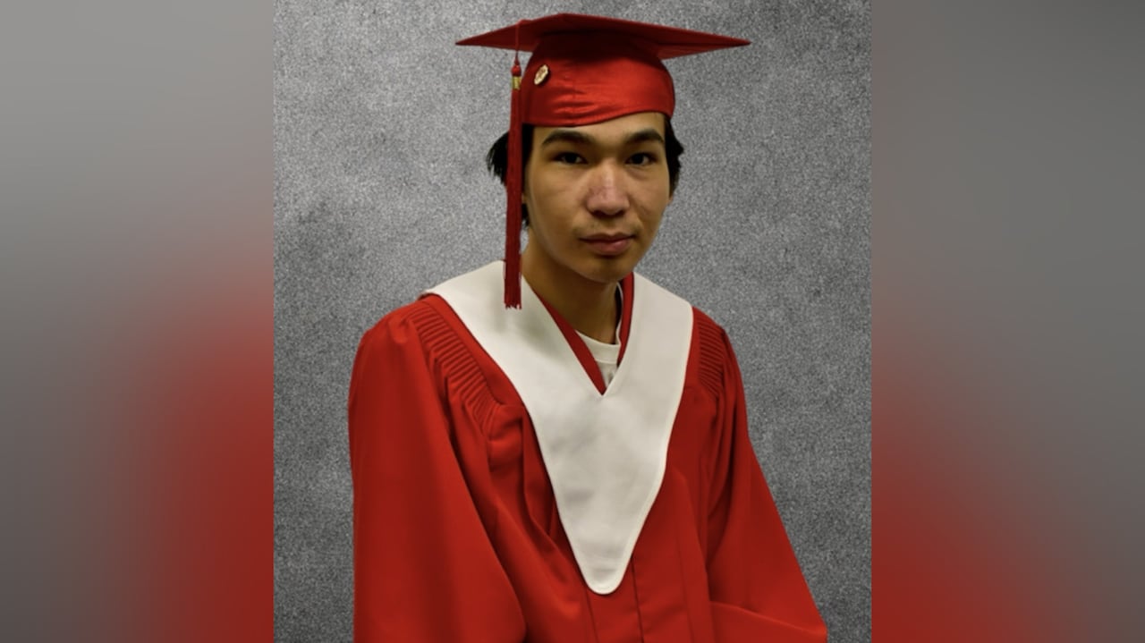 A man wearing a red graduation cap and gown looks to the camera.