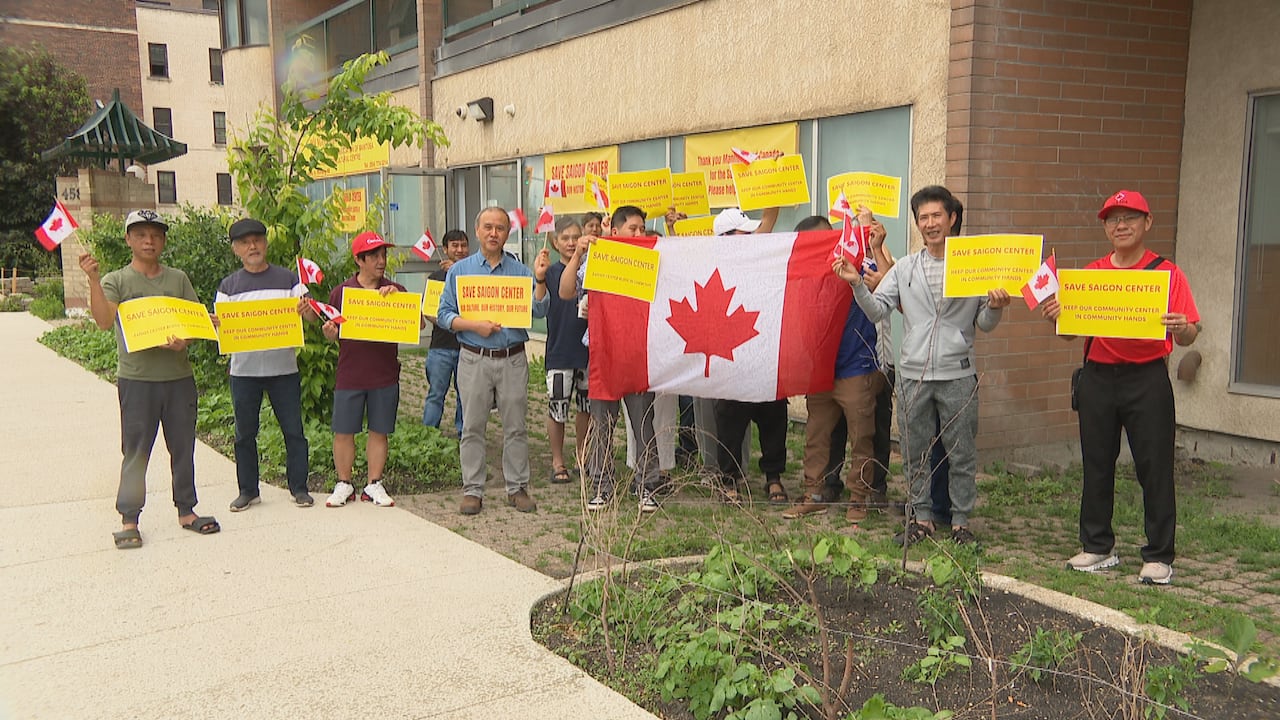A group of people hold up Canadian flags and signs that say "Save Saigon Centre."
