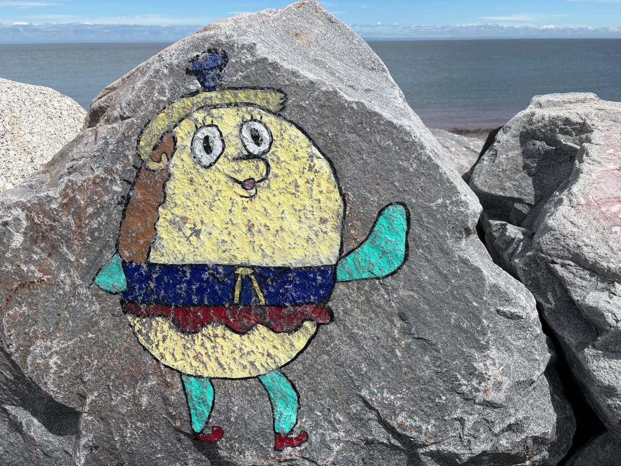 A cartoon painting of a pufferfish is painted on a rock.