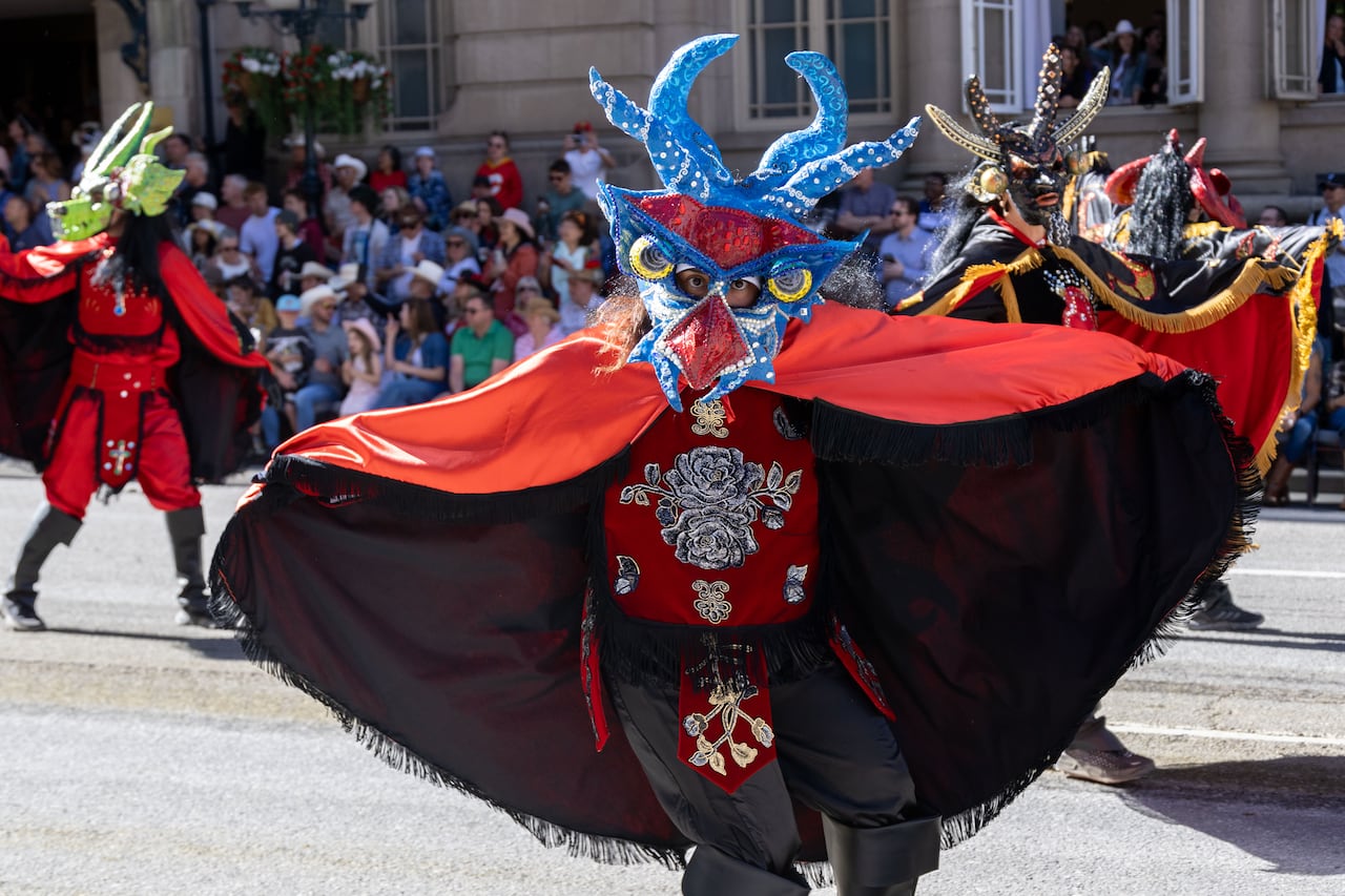 A person in a parade wearing a mask and cape.