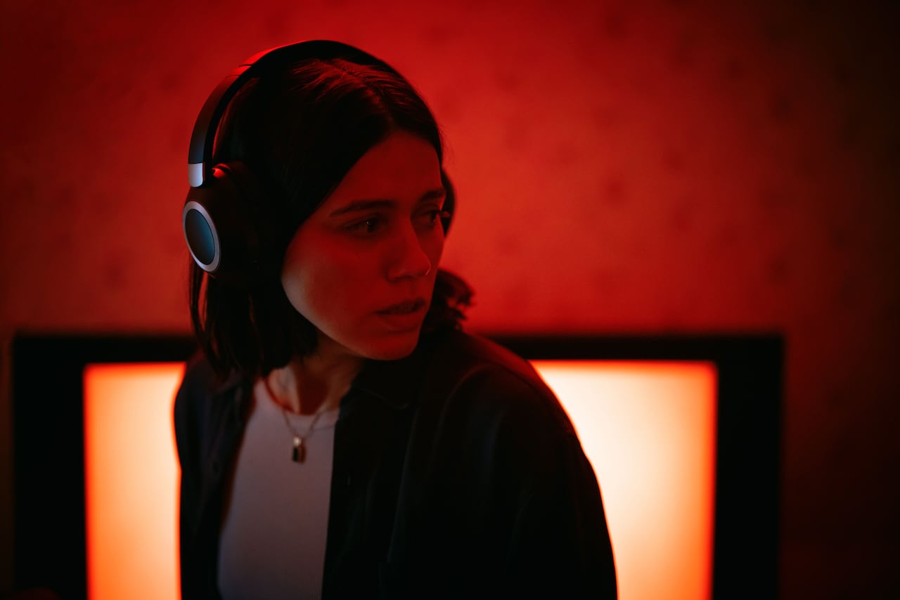 Standing in front of an orange glow, a woman with medium-length hair wears headphones.