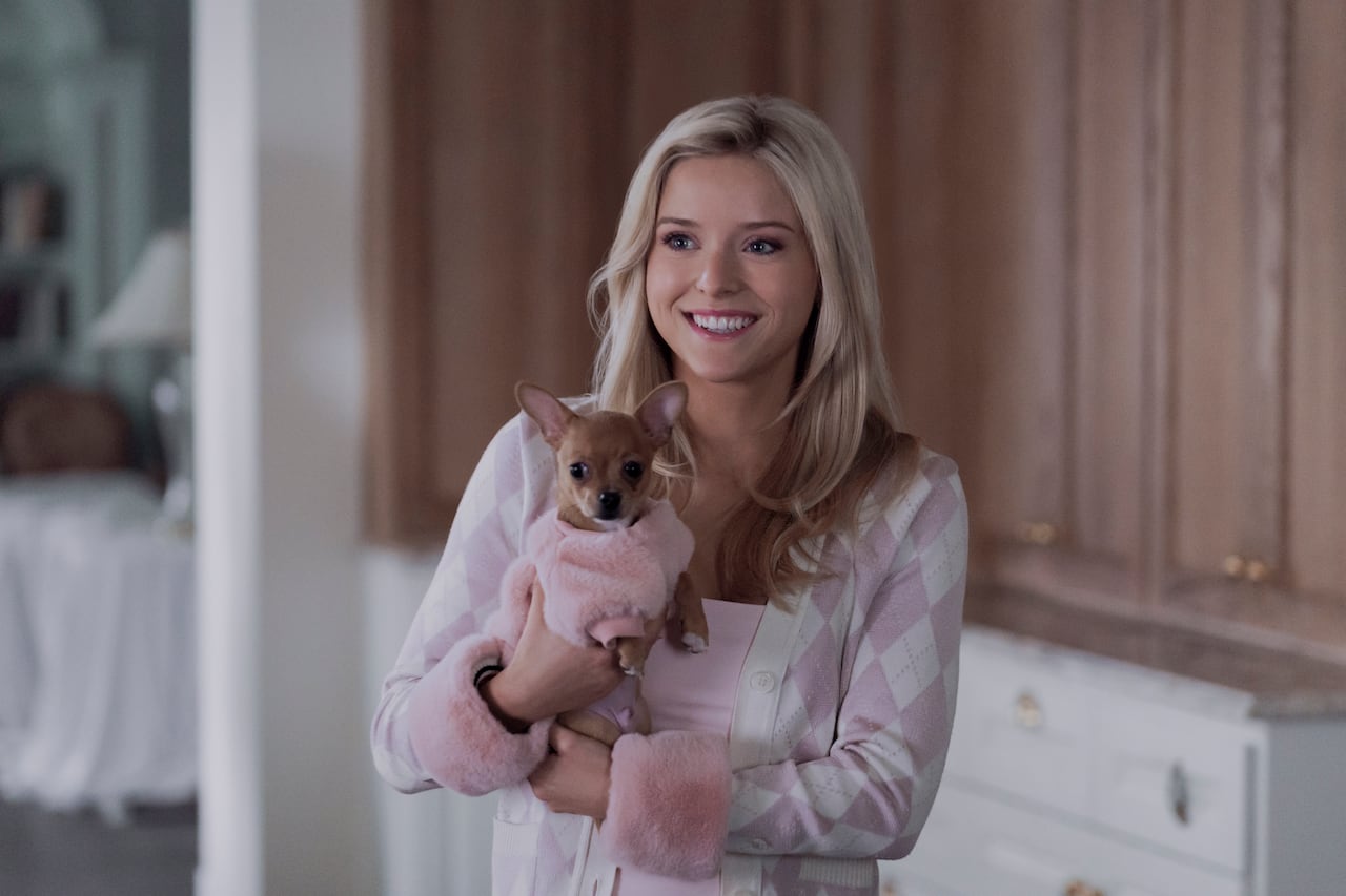 A woman wearing pink smiles while holding a small dog in a pink sweater.