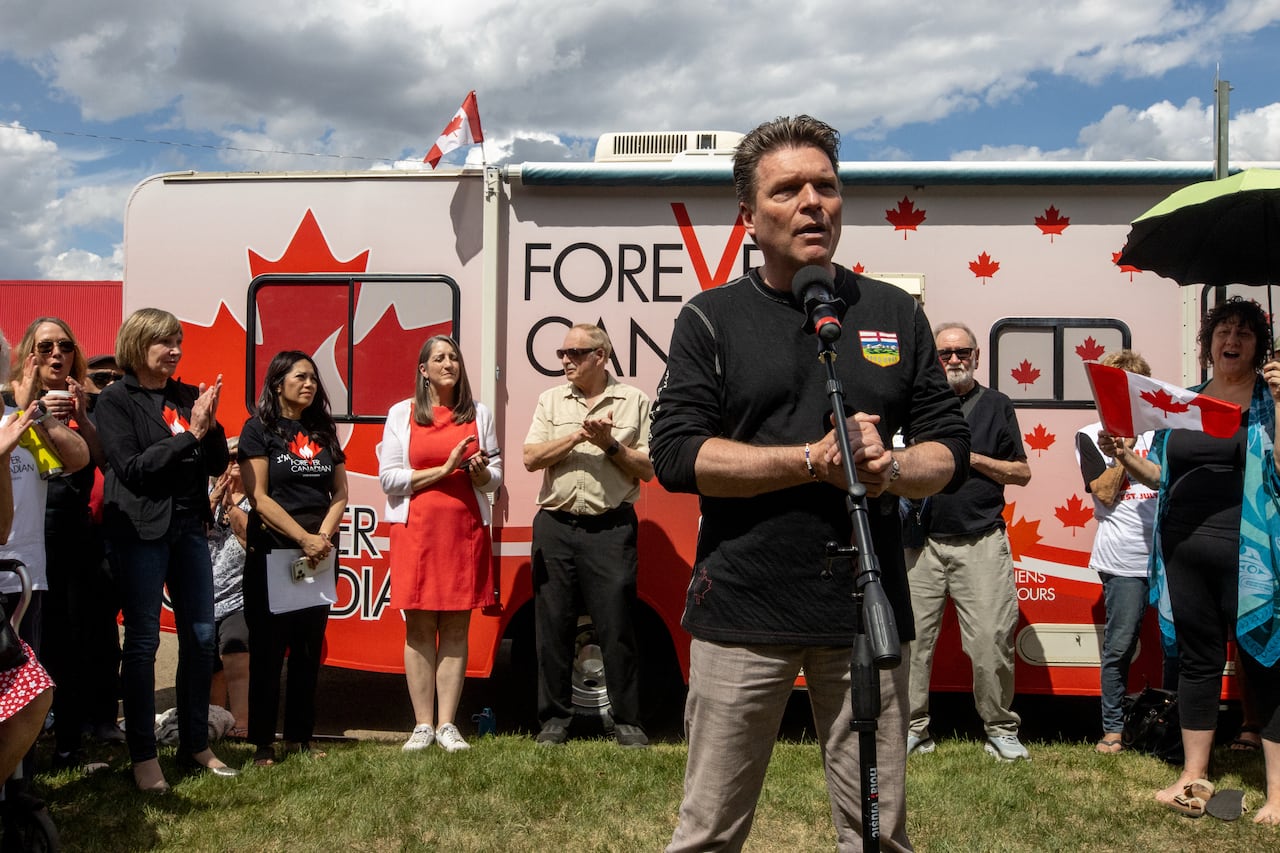 A man stands in front of a bus that is covered in red maple leaves.