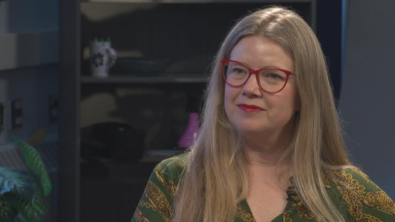 A woman wearing red glasses looks at the camera.