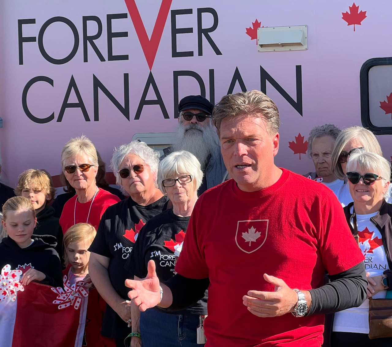 A man in a red shirt with a maple leaf on it stands in front of a crowd of people in similar red and black shirts.