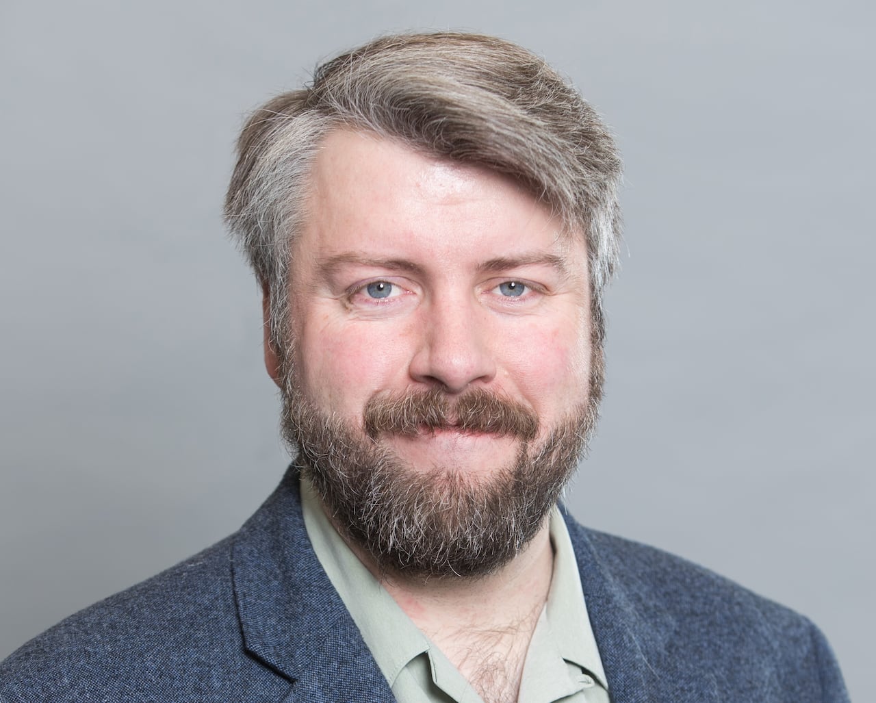 A man in a blue blazer and beige shirt poses for a portrait.