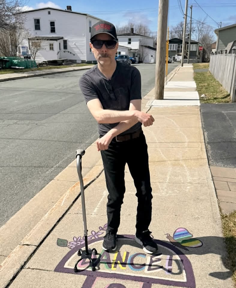 A man with a cane standing on a piece of sidewalk art that says "dance."