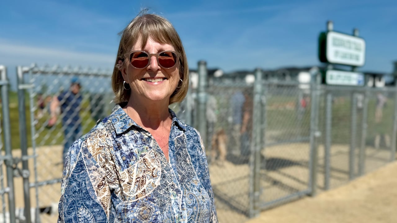 A woman smiles at the camera. Behind her there's a fenced-in area.