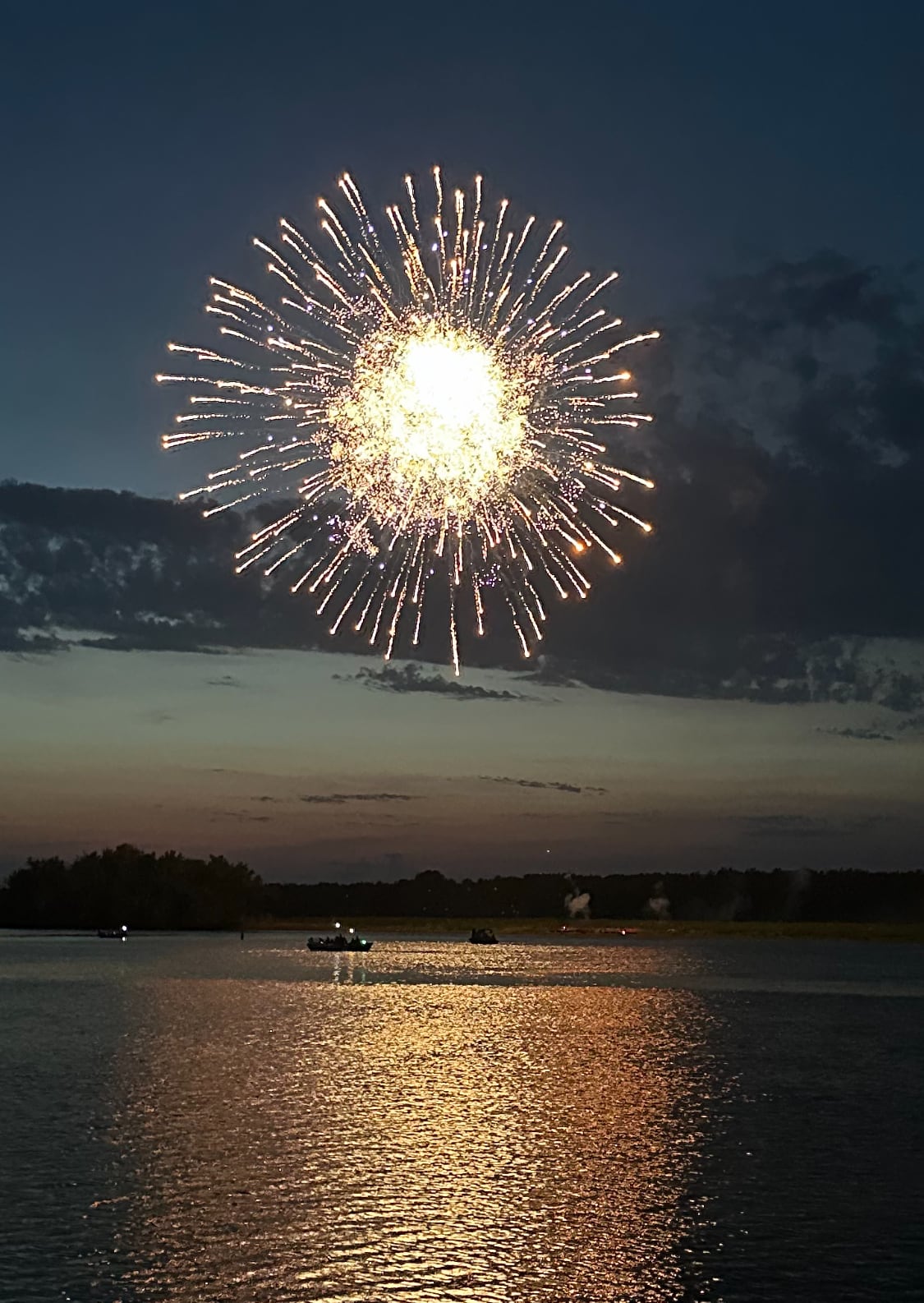 Golden fireworks explode over a river at night time.