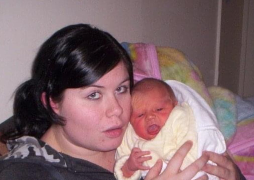 A woman with black hair holds up a crying baby.