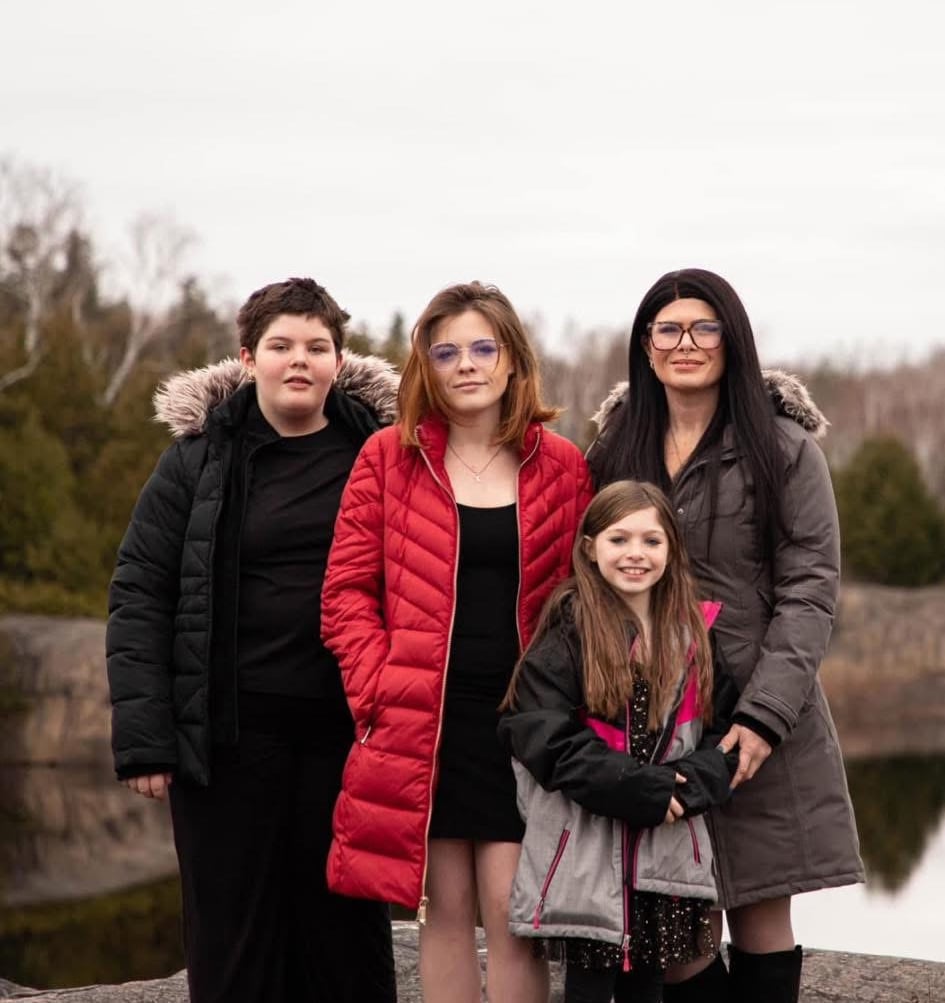 A smiling woman stands next to three girls.