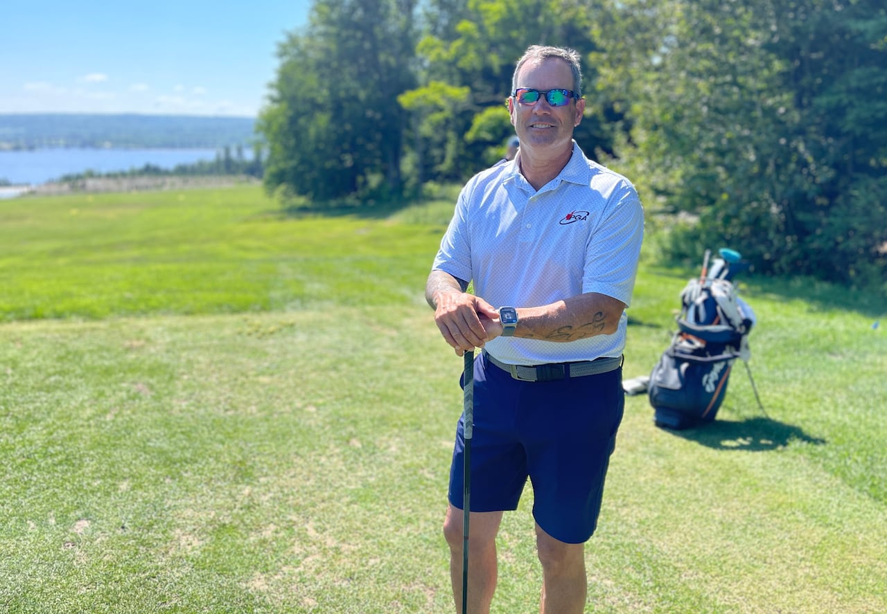 A man in a white shirt and blue shorts posing with a golf club.