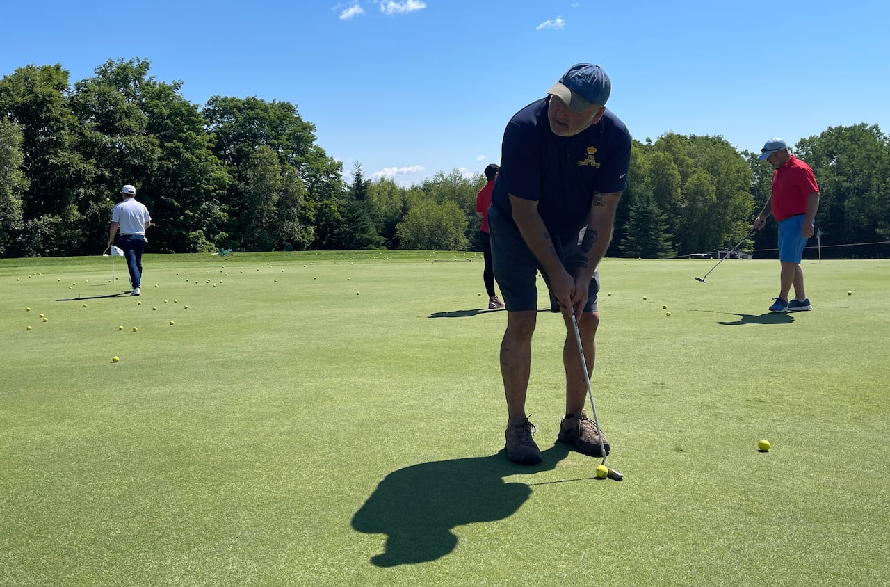 A man standing over a golf ball putting on a golf green.