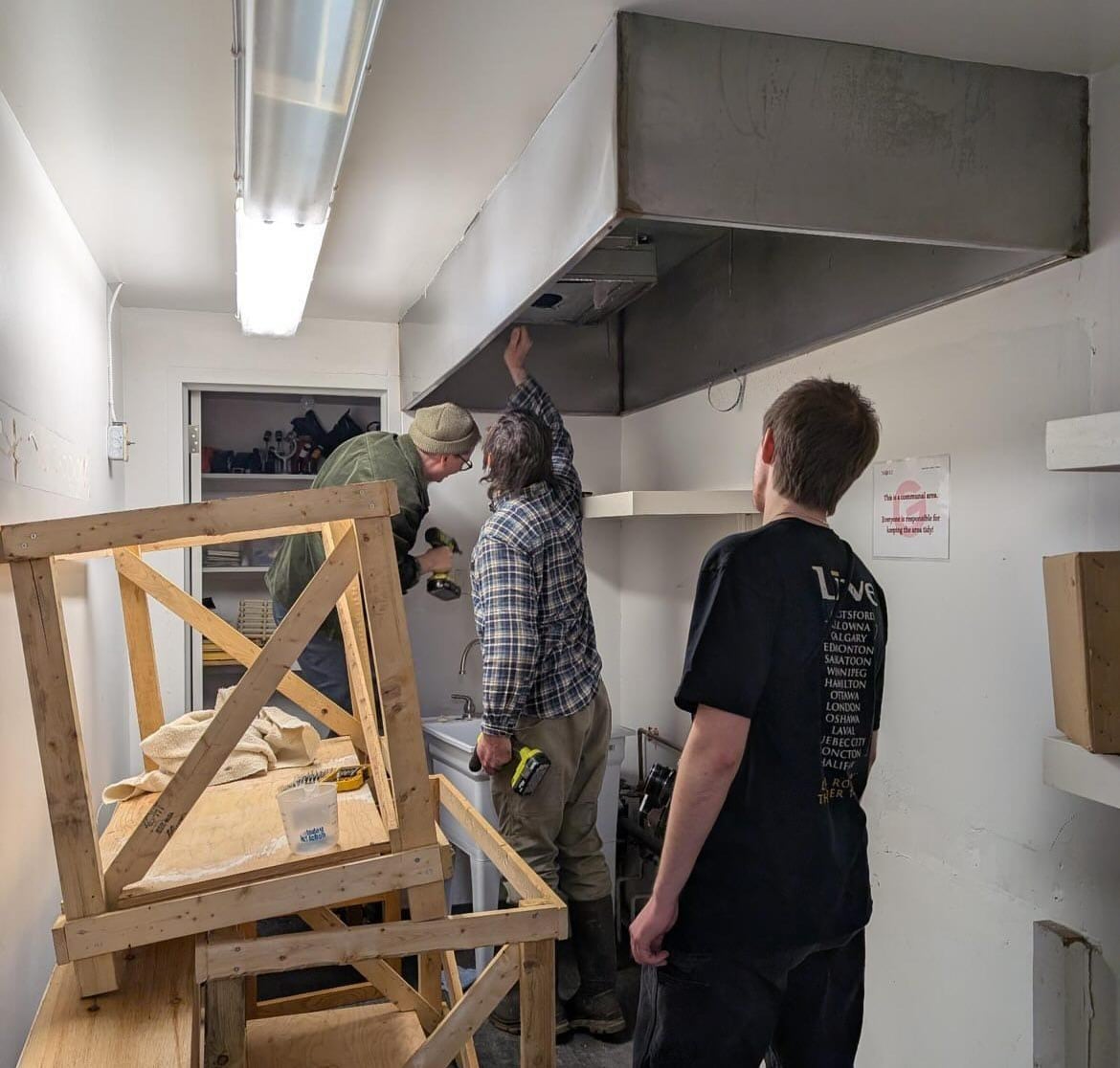 Three people in a cluttered room with strip lighting doing some construction work